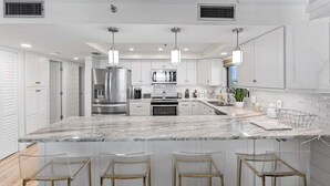 A modern kitchen with white cabinetry, a marble island, stainless steel appliances, and pendant lighting.