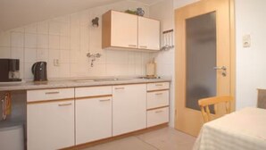 Een compacte keuken met witte kastjes, een koffiezetapparaat en een deur met een geëtste glazen ruit.