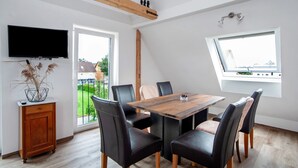 Ein Essbereich mit Holztisch, schwarzen Stühlen, einem an der Wand befestigten Fernseher und einem Fenster mit Blick nach draußen.