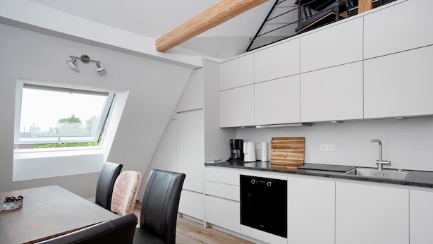 Eine moderne Küche mit weißen Schränken, einem schwarzen Geschirrspüler und einem Fenster mit Blick auf Grünflächen.