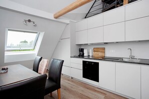 Moderni keittiö, jossa on valkoiset kaapit, musta astianpesukone ja ikkuna, josta avautuu näkymä vehreään maisemaan.