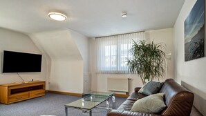 Un salón con una mesa de centro de vidrio, un sofá de cuero, un mueble de entretenimiento de madera y un ventanal con cortinas.