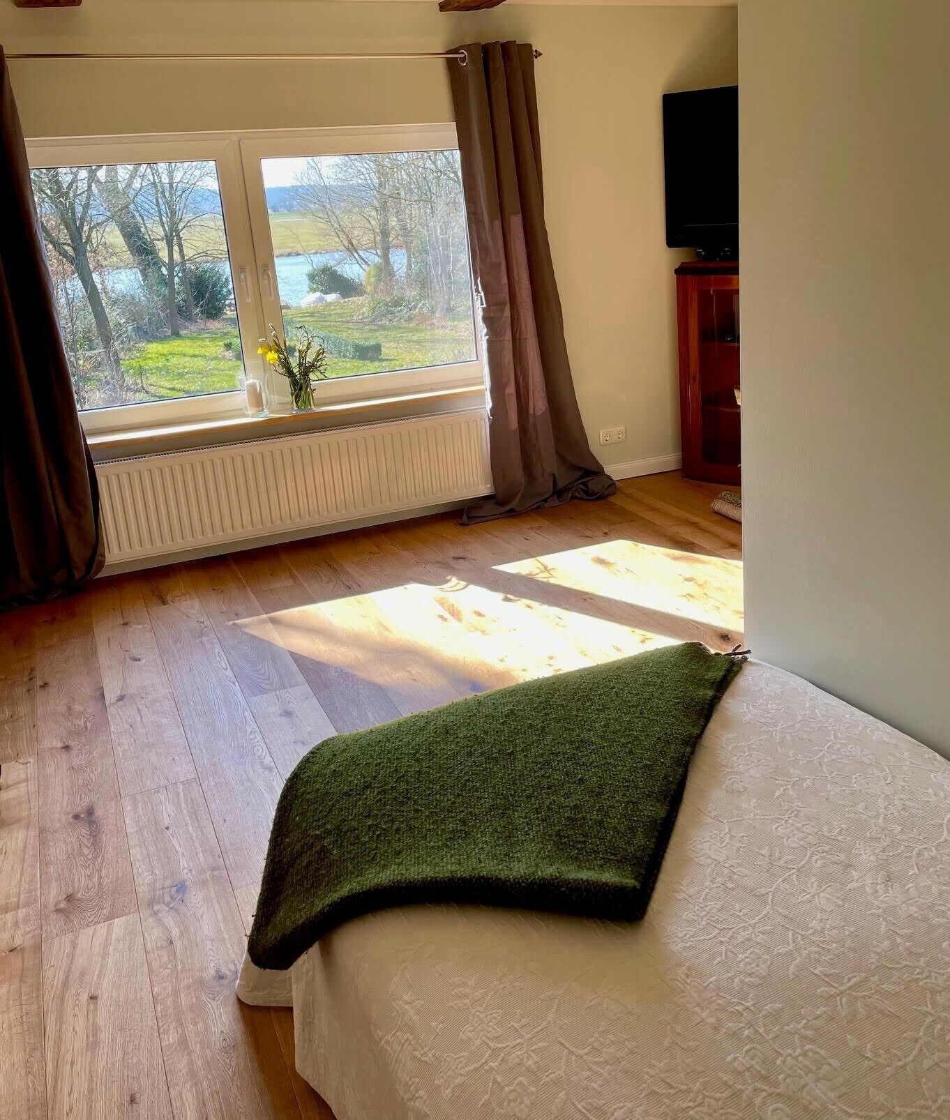 Ein Schlafzimmer mit Bett, einem fensterbehangenen Fenster, einem Heizkörper und einem Fernseher.
