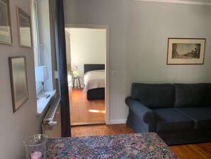 A room with a bed, a sofa, a table with a patterned tablecloth, and a framed picture on the wall.