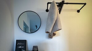 A room with a black console table, a round mirror, a towel rack, a small stool, and a framed welcome sign.
