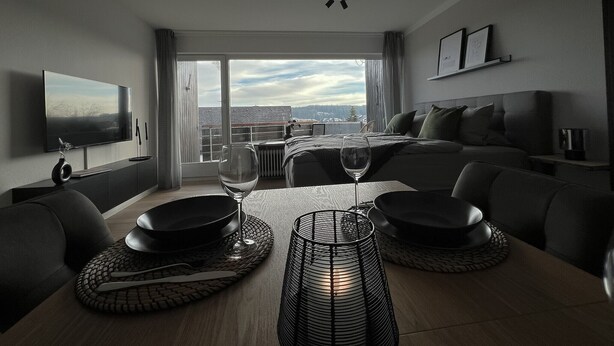 A modern hotel room with a dining area, a bed, and a TV.