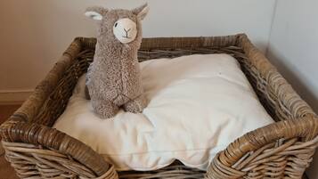 Un panier en osier contenant un doudou en forme d’agneau, posé sur un coussin blanc.