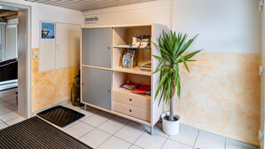 Un'area di accoglienza con una porta chiusa, una pianta in vaso, uno scaffale con brochure e un pavimento piastrellato.