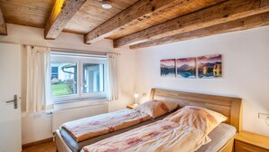 Una camera da letto con due letti, travi in legno a vista, una finestra con tende e un muro decorato con tre dipinti di paesaggi.
