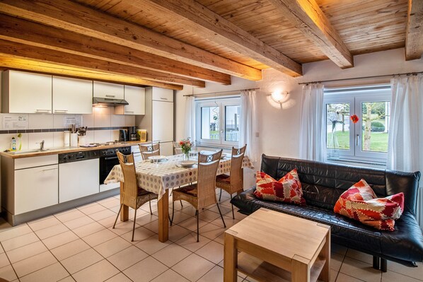 A modern kitchen with white cabinets, a dining table with chairs, a black leather sofa, and a wooden coffee table.
