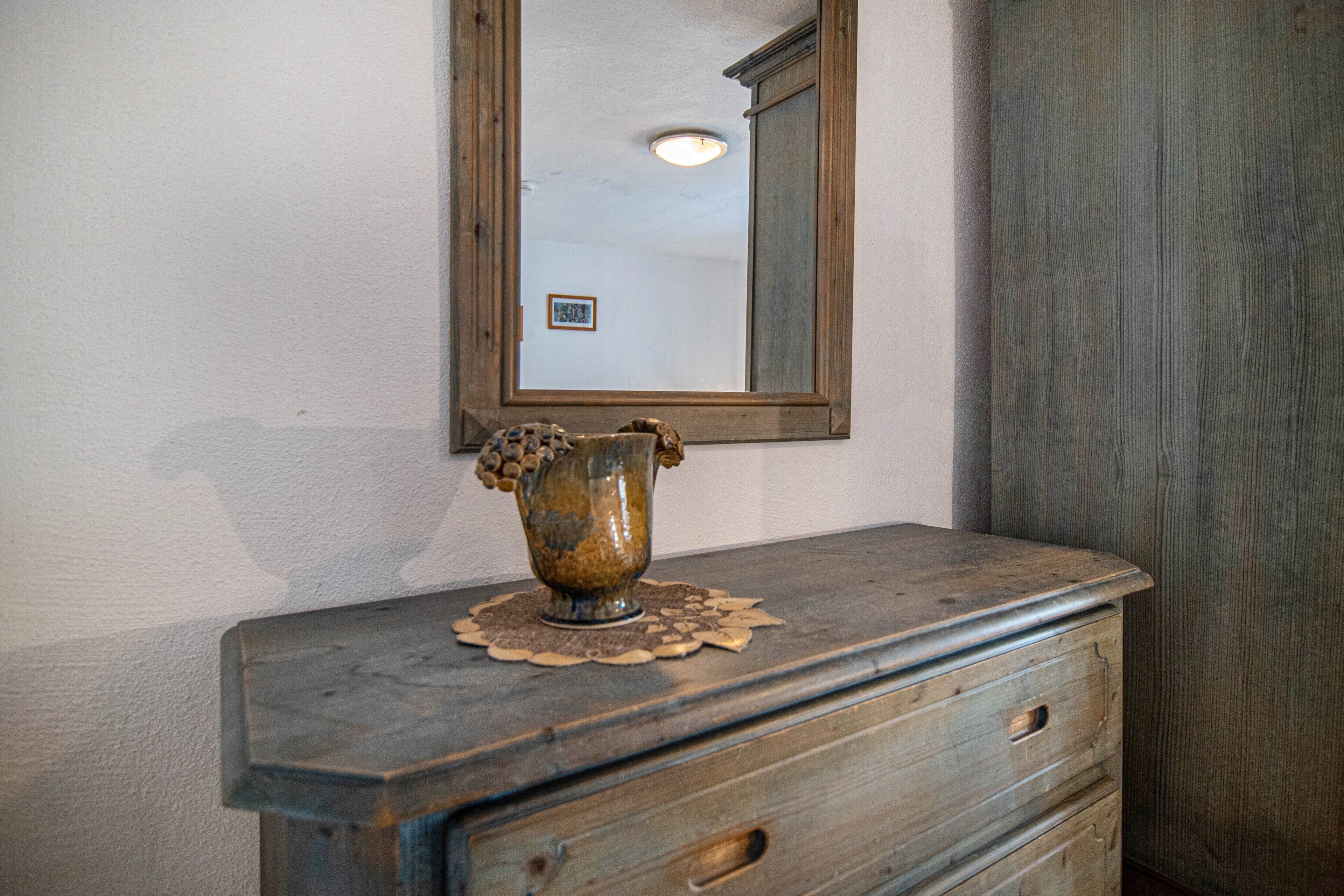 Une commode en bois sur laquelle est posé un vase, un miroir au-dessus et une porte en bois sur le côté droit.