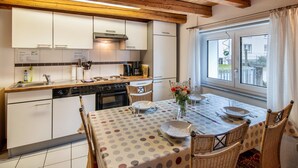A kitchen with white cabinets, a dining table with a polka dot tablecloth, wicker chairs, and a window with a view of the outside.