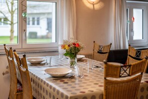 A dining table with a polka dot tablecloth, surrounded by wicker chairs, and a vase with flowers.