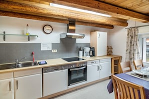 Una cucina con lavello, fornello, forno e pensili bianchi. Si vede un orologio appeso al muro e una finestra con tende.