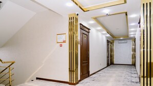 A hallway with a marble floor, a wooden door, and a staircase with golden railings. - PGA Hotel (Tashkent)
