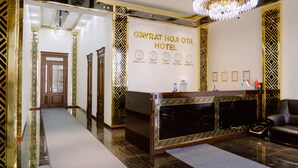 A reception area with a reception desk, a chandelier, and a wall displaying the hotel name and location. - PGA Hotel (Tashkent)