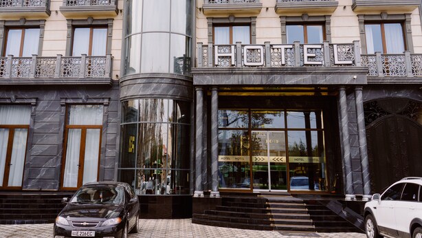 A hotel entrance with a grand facade, large glass windows, and a prominent "HOTEL" sign. - PGA Hotel (Tashkent)