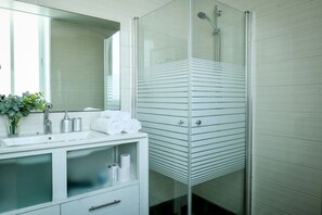 A modern bathroom with a glass shower enclosure, a white vanity with a mirror, and a small plant on the counter. - The Printhouse-Boutique Apt by SeaNRent  (Haifa)