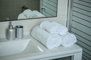 Une salle de bain avec un lavabo blanc, deux flacons argentés et trois serviettes blanches soigneusement pliées.