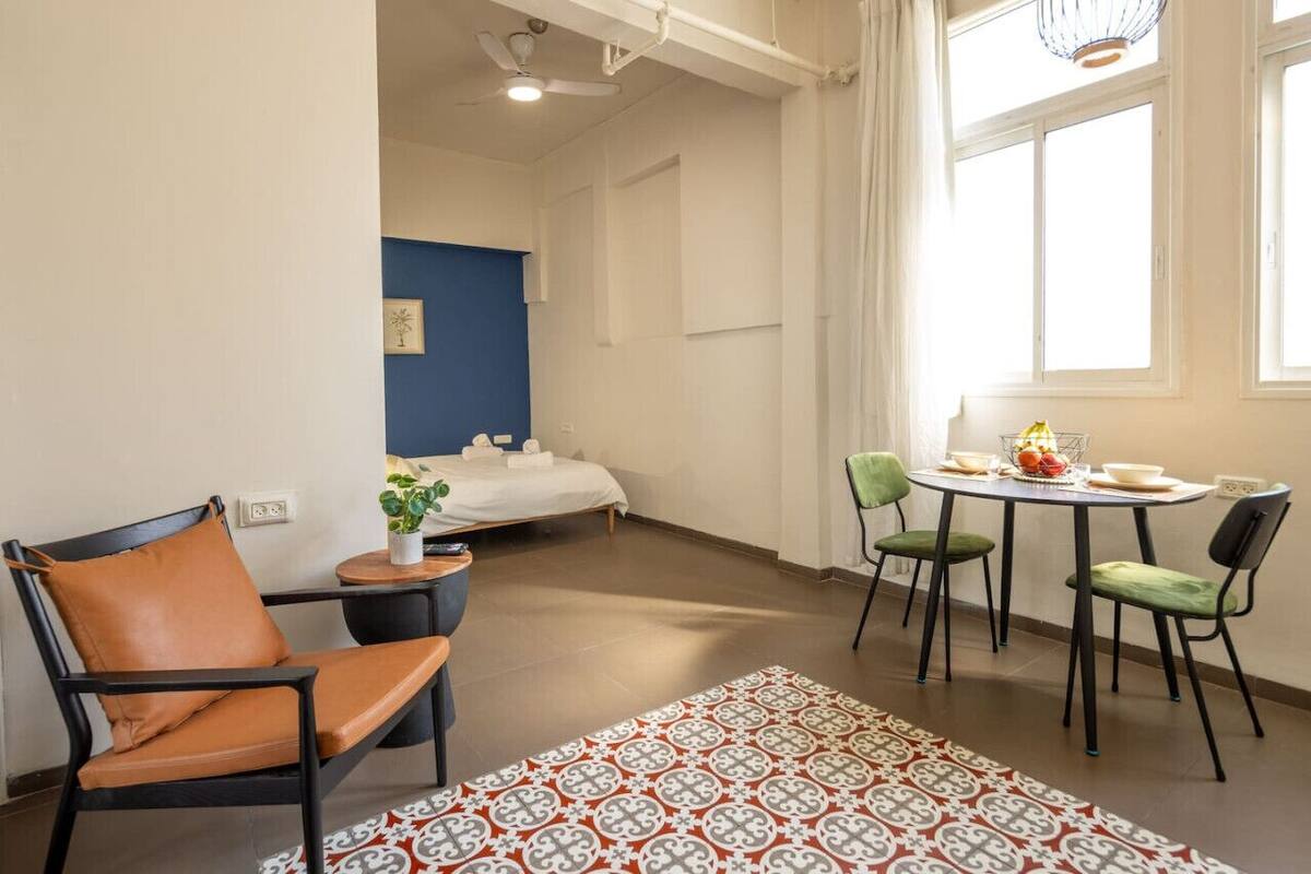 A hotel room with a bed, a small table with chairs, a plant, and a window with curtains.