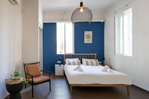 Ein Schlafzimmer mit Bett, Sessel, Nachttisch, Pendelleuchte und Fenster.