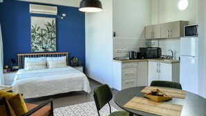 Habitación de hotel compacta con cama, una kitchenette pequeña, un área de comedor con mesa y sillas, y una pared azul de acento.