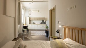 Una habitación de hotel moderna con una cama, una mesita de noche, una lámpara y vistas a una cocina y zona de comedor.