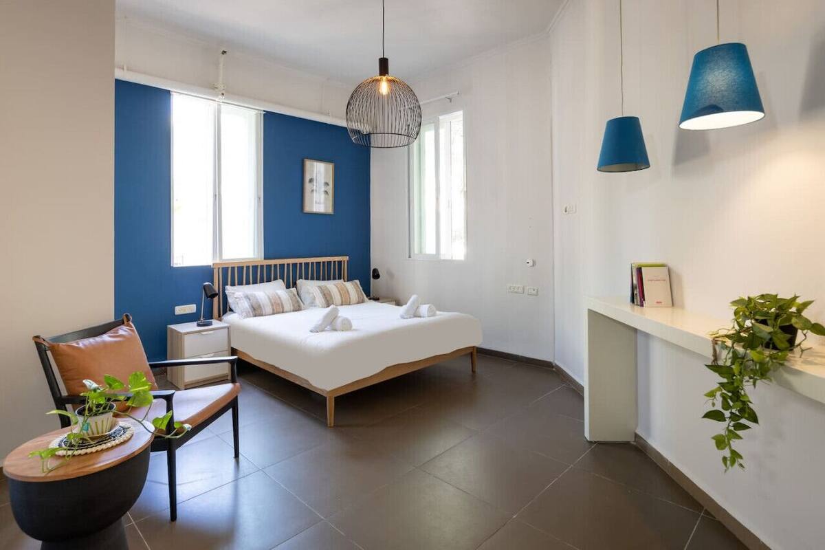 A modern bedroom with a bed, bedside tables, a chair, a hanging light fixture, and a window.