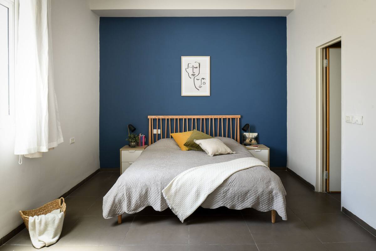 A bedroom with a bed, a bedside table, a wall art piece, and a window with curtains.