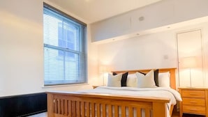 Ein Schlafzimmer mit einem hölzernen Bett, einem Fenster mit Jalousien, einer Heizung und einem Nachttisch mit Lampe.