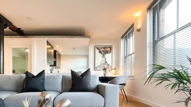 Ein modernes Wohnzimmer mit einem grauen Sofa, schwarzen Kissen, einem metallenen Couchtisch und Holzboden.