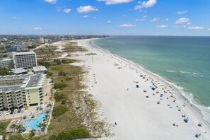 A beach resort with a large pool, beachfront umbrellas, and a view of the ocean. - Your Dream Getaway in Treasure Island. Heated Pool. Beachfront Tiki Bar. Hot Tub. On-site Cafe. (Treasure Island)