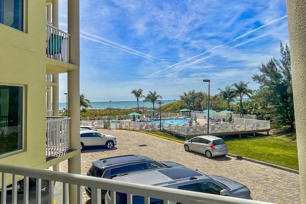 A view of a pool area with a clear sky, palm trees, and a beach in the background. - Your Dream Getaway in Treasure Island. Heated Pool. Beachfront Tiki Bar. Hot Tub. On-site Cafe. (Treasure Island)