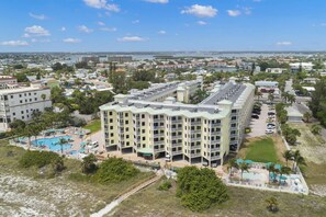 A multi-story hotel with a pool area, surrounded by greenery and a view of the sea. - Your Dream Getaway in Treasure Island. Heated Pool. Beachfront Tiki Bar. Hot Tub. On-site Cafe. (Treasure Island)