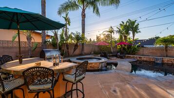 An outdoor patio with a stone fire pit, seating, and a small water feature.