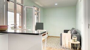 A modern kitchen with a central island, a dining area with a sofa and a small table, and a living area with a grey sofa and a blanket. - Atlantic View, a Home in Madeira (Ponta do Sol)