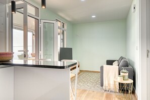 A modern kitchen with a central island, a dining area with a sofa and a small table, and a living area with a grey sofa and a blanket. - Atlantic View, a Home in Madeira (Ponta do Sol)