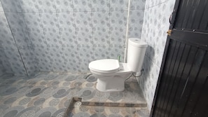 A bathroom with a toilet, patterned tiles, and a drain. - OYO 93603 Nurbata Holdings (Mertak)