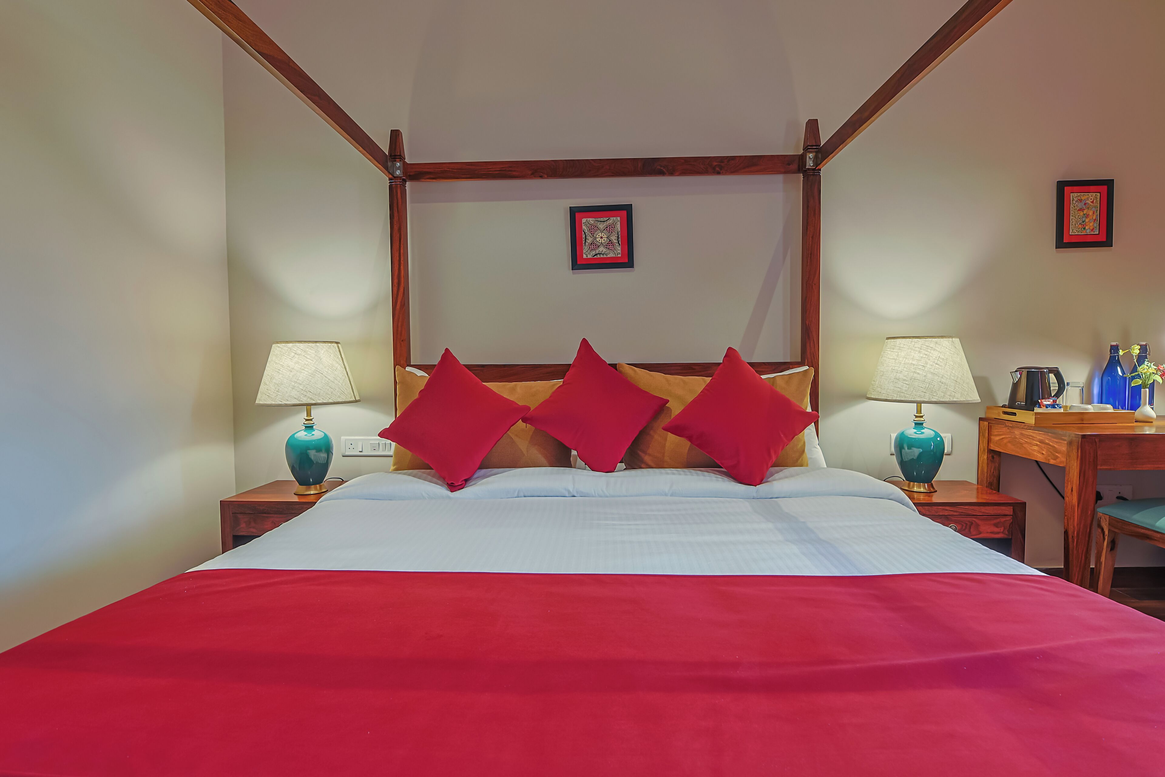 Una habitación de hotel con cama con dosel, ropa de cama roja y blanca, dos lámparas y un escritorio de madera con una silla.