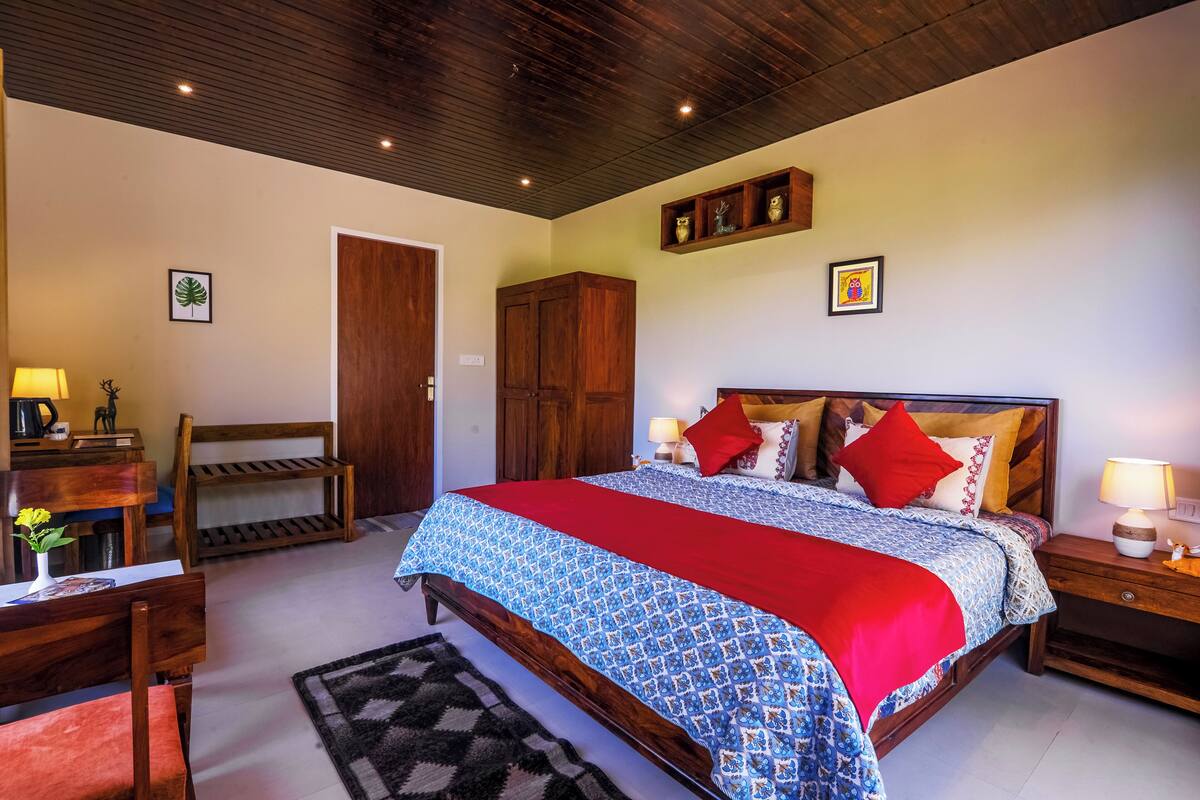 Une chambre avec un lit en bois, une literie rouge et bleue, une table de chevet en bois, un bureau avec une lampe et une chaise.