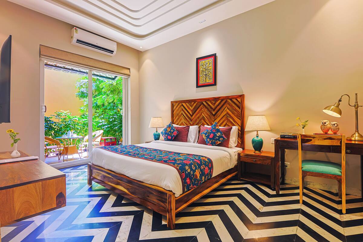 Une chambre à coucher comprenant un lit, des tables de chevet, un bureau et une chaise. Une fenêtre offre une vue sur la verdure environnante.