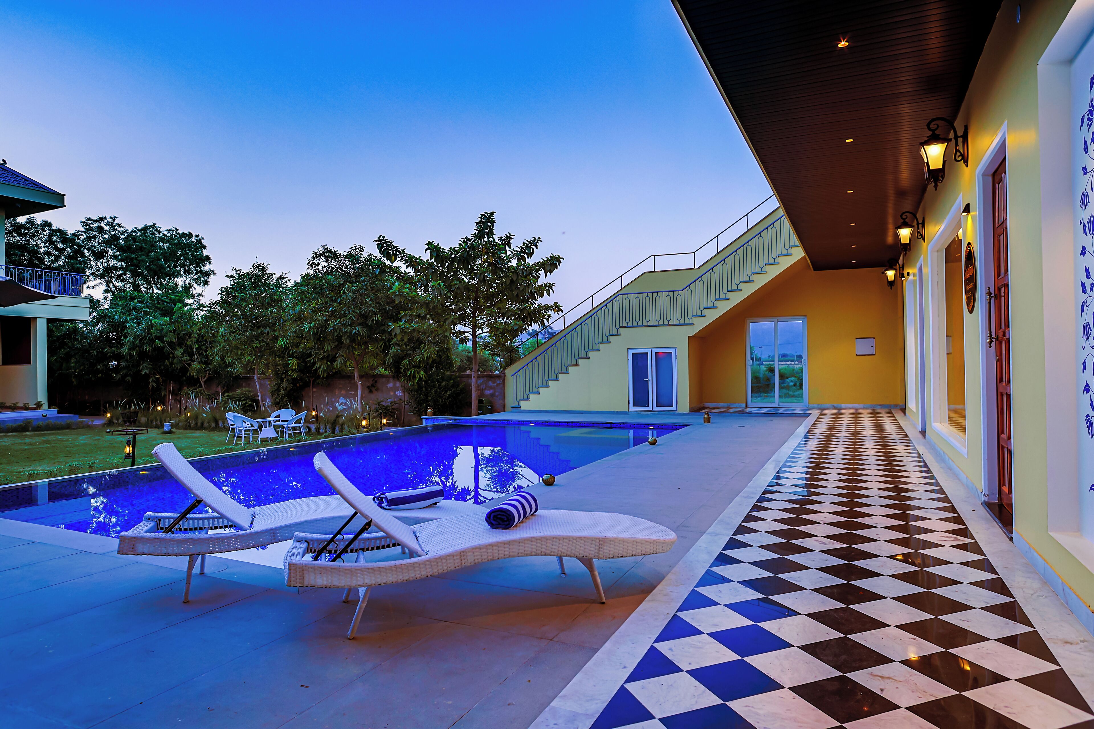 A pool area with lounge chairs, a checkered floor, and a staircase leading to a building.