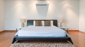 A modern bedroom with a large bed, two bedside tables, a wall-mounted air conditioner, and a fluffy rug. - Phuket Cleanse (Rawai)