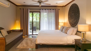 A bedroom with a bed, a sofa, a ceiling fan, a wall-mounted air conditioner, and a large window with curtains. - Phuket Cleanse (Rawai)