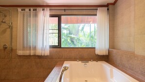 A bathroom with a large bathtub, a shower, and a window with curtains. - Phuket Cleanse (Rawai)