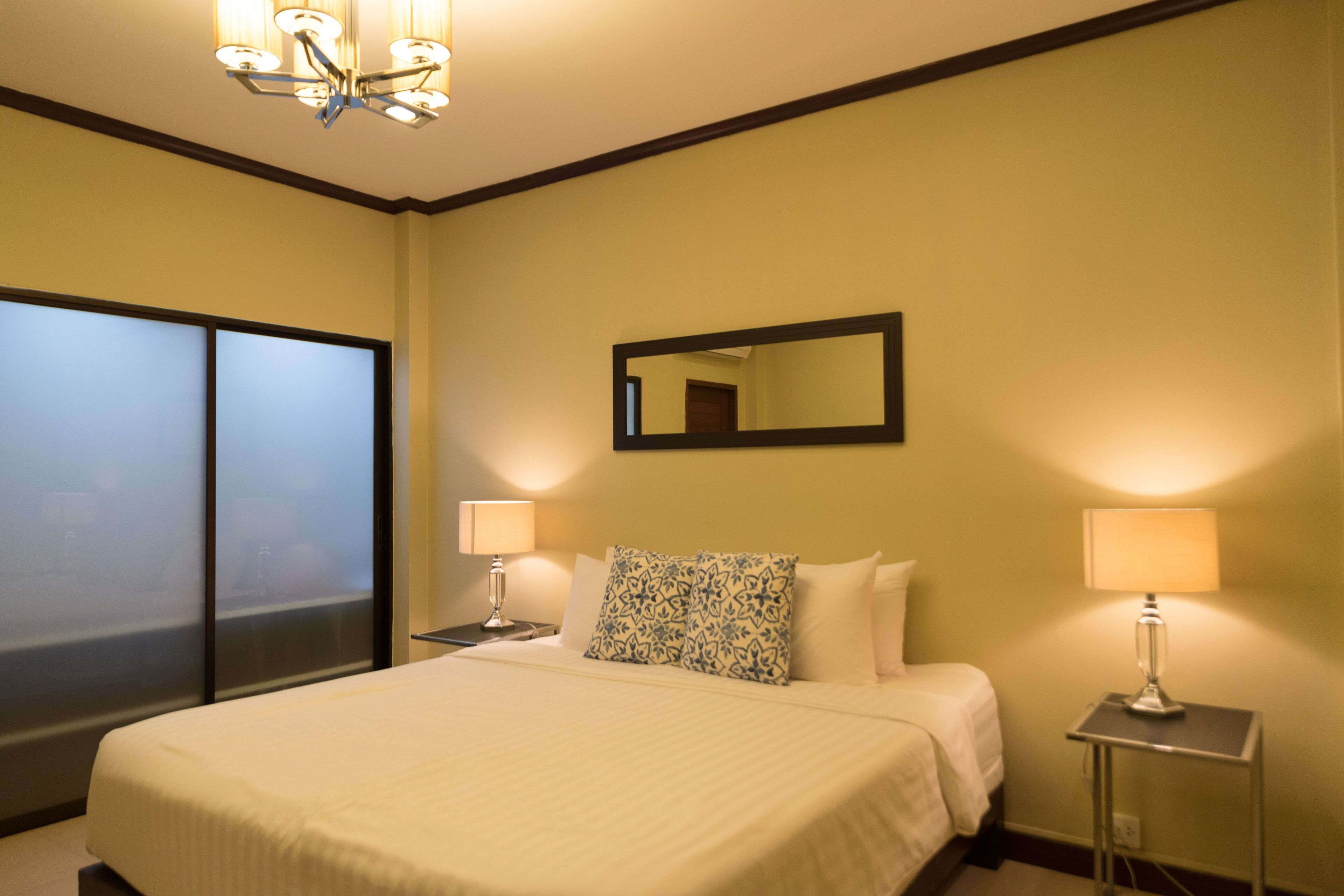 A hotel room with a large bed, two bedside tables with lamps, a mirror on the wall, and a view through a large window.