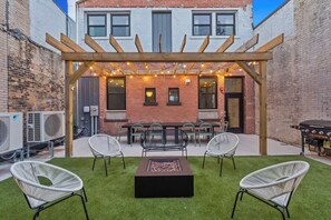 An outdoor patio with a pergola, string lights, a fire pit, and white wicker chairs. - Downtown 5BR with private patio (Grand Rapids)