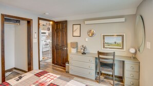 Une chambre à coucher comprenant un lit, une commode, une chaise, un bureau et un miroir. Une porte donne accès à une autre pièce.