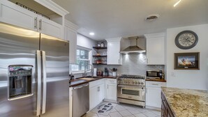 A modern kitchen with stainless steel appliances, white cabinetry, a granite countertop, and a tiled floor. - Poolside Paradise! Central Merritt Island Home (Merritt Island)