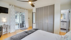 A bedroom with a bed, a ceiling fan, a TV, a wardrobe, and a bathroom visible through a glass door. - Poolside Paradise! Central Merritt Island Home (Merritt Island)